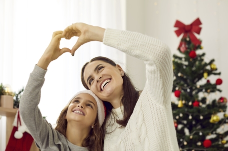 mother and daughter making heart shape with hands in front of Christmas tree